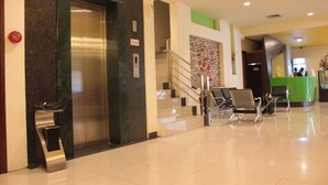 A lobby with a reception desk, a staircase, and a reception area with chairs. - Jolin Hotel (Makassar)