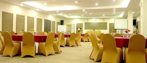 A conference room with rows of tables and chairs, equipped with a projector screen and a whiteboard.