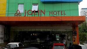 A hotel with a green and blue facade, a red entrance, and the name "JOLIN HOTEL" displayed. - Jolin Hotel (Makassar)