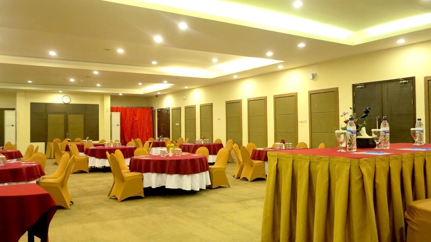 A conference room with round tables, yellow chairs, and red tablecloths.