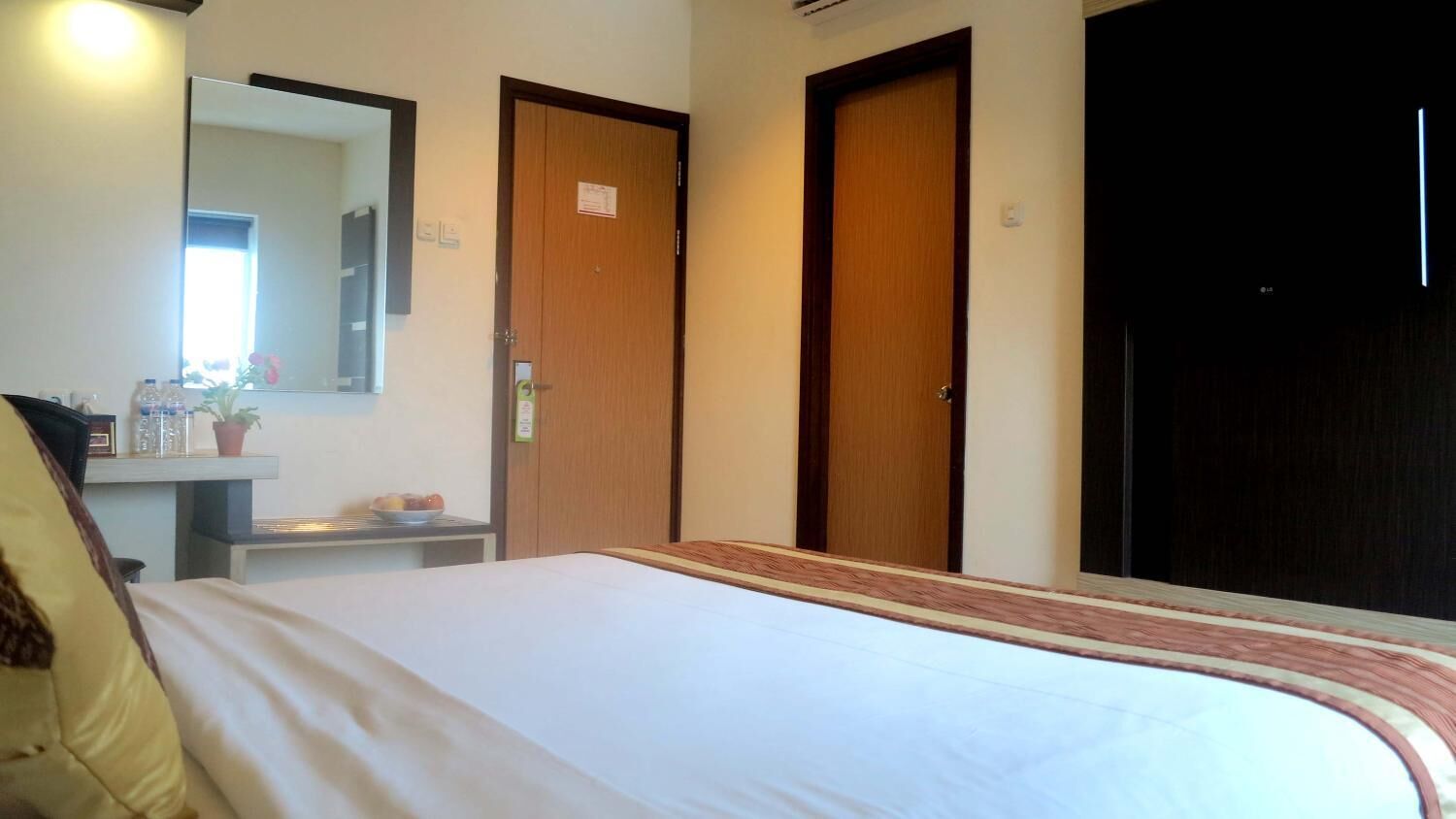 A hotel room with a bed, a bedside table with toiletries, a mirror, and two doors.