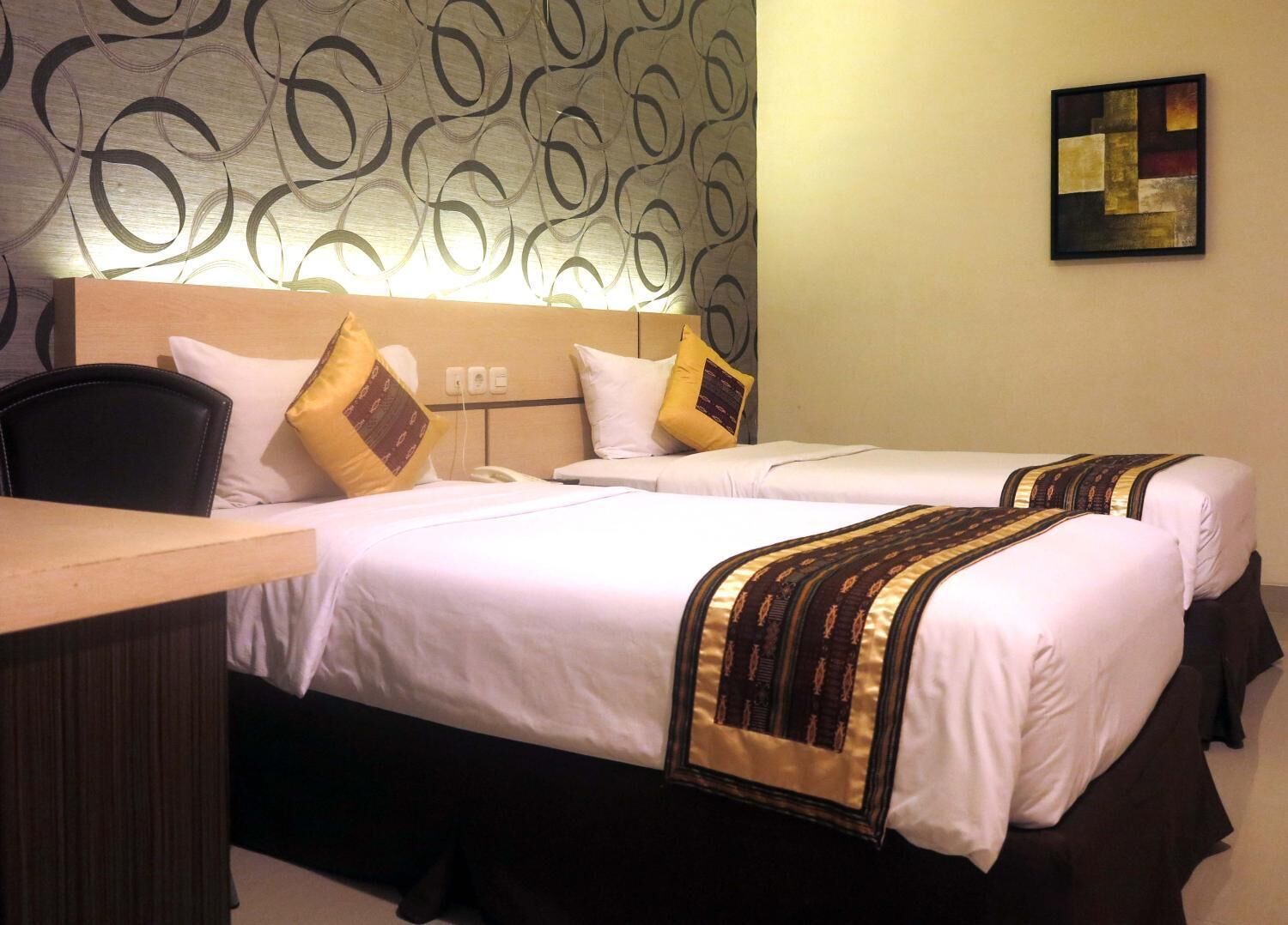 Quarto de hotel com duas camas, uma escrivaninha e papel de parede estampado.