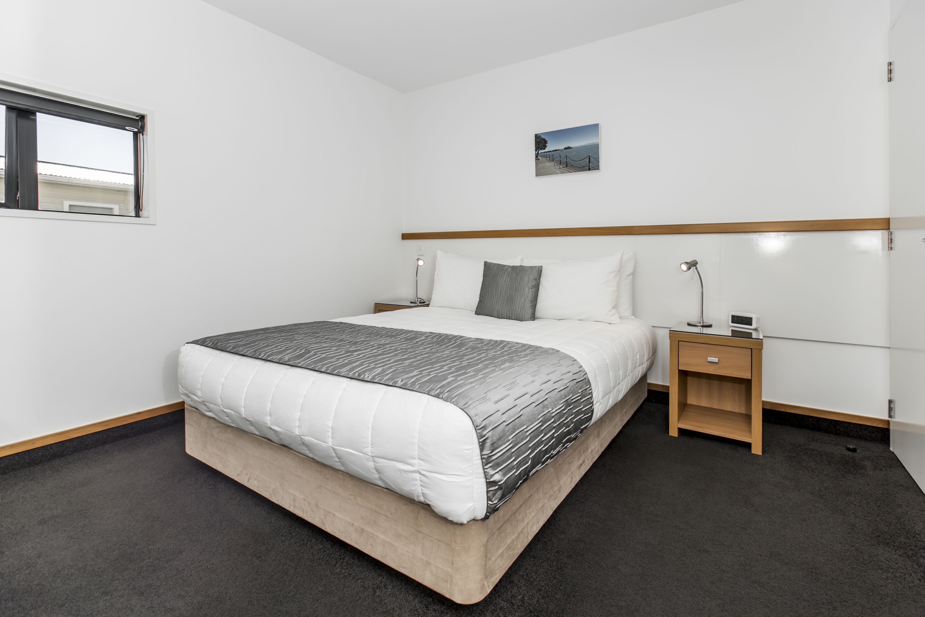 A neatly arranged hotel room with a bed, bedside tables, a nightstand, and a window.
