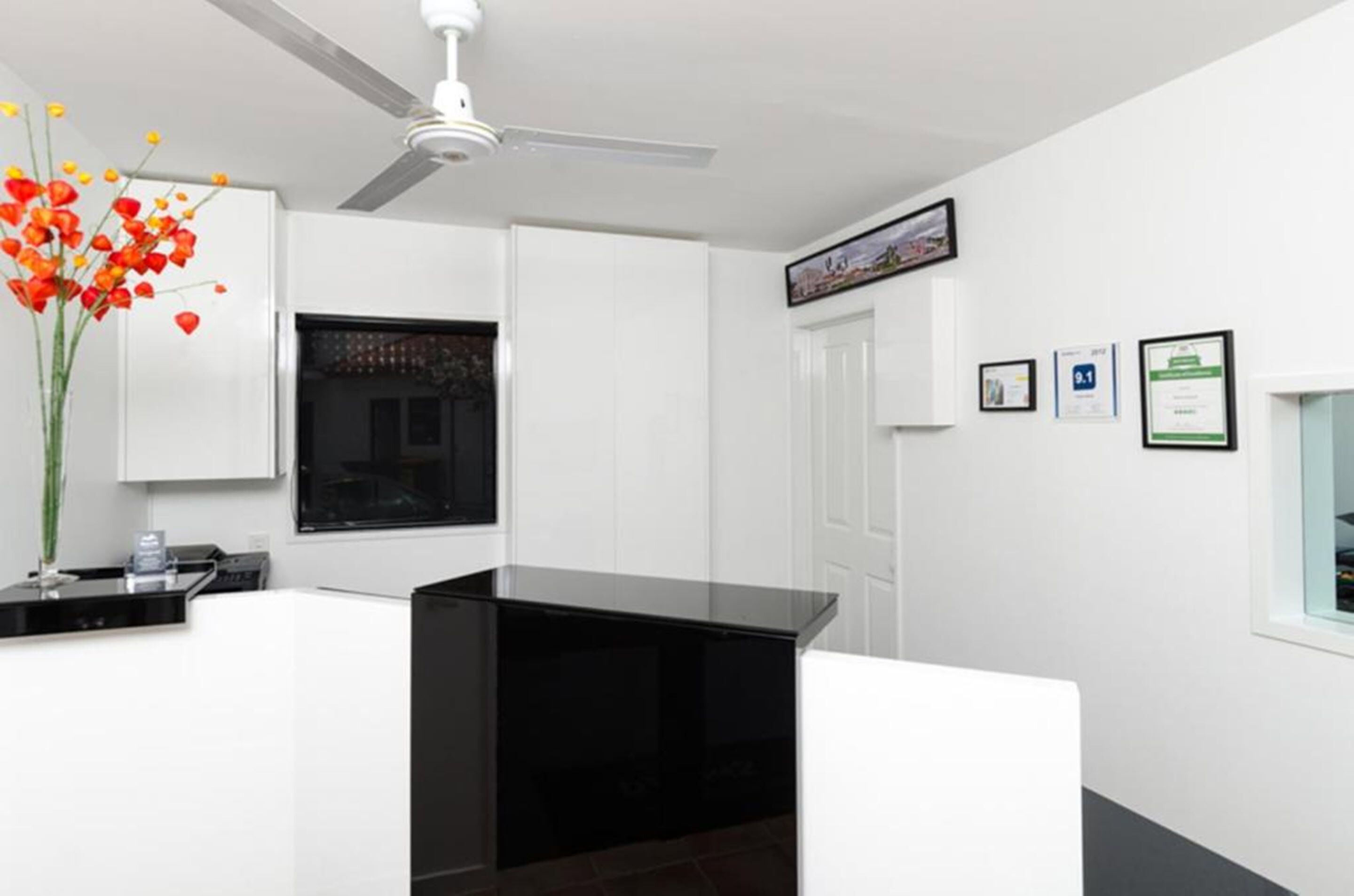 Une cuisine moderne avec des meubles blancs, un plan de travail noir et un ventilateur de plafond.