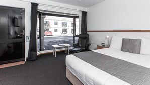 Une chambre d’hôtel avec un grand lit, un bureau, une chaise, une fenêtre avec des rideaux et une vue sur la rue.