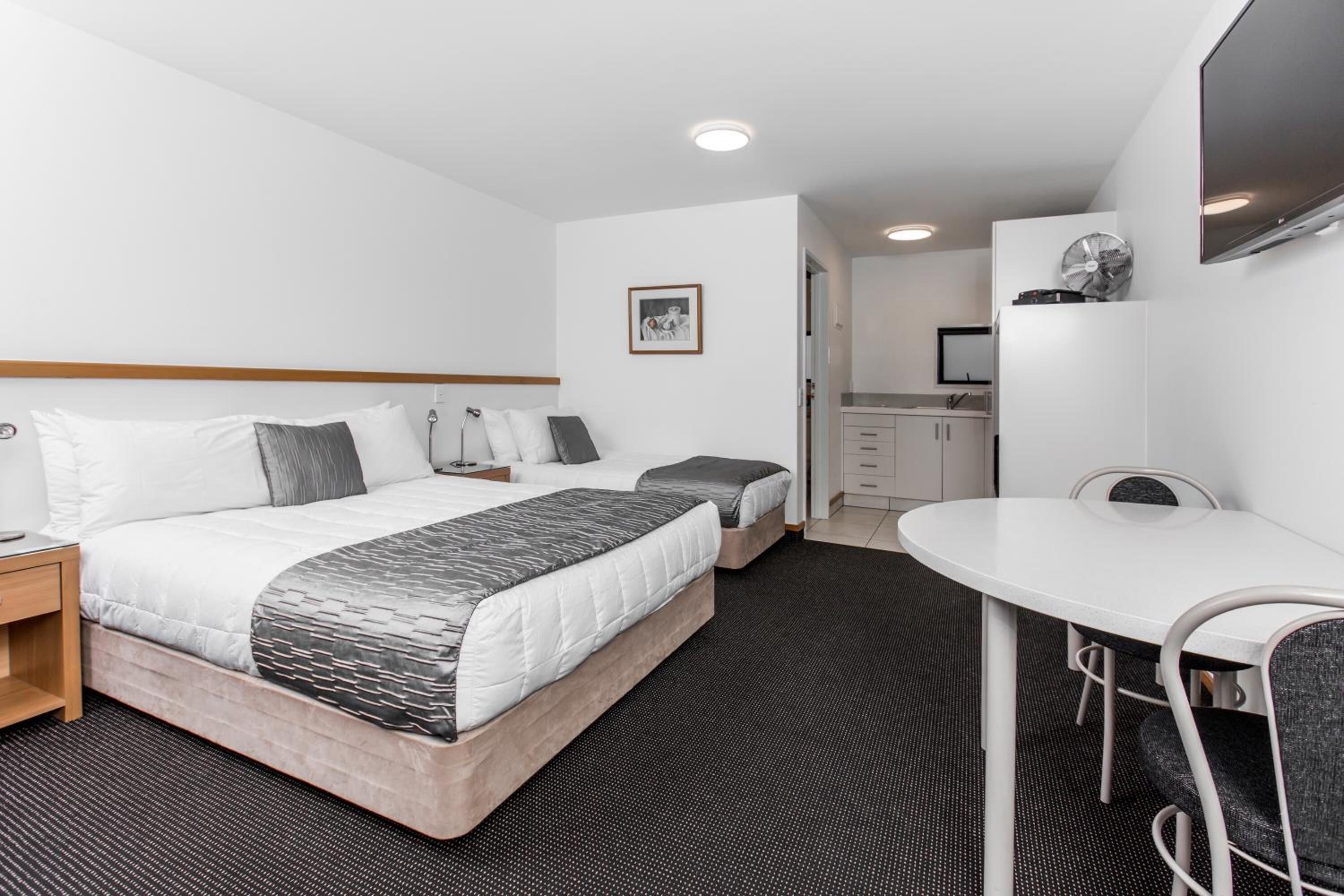 A hotel room with a bed, bedside tables, a desk, a chair, a TV, and a kitchenette.