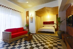A hotel room with a checkered floor, a red sofa, a bed with a red headboard, and a large window with curtains.