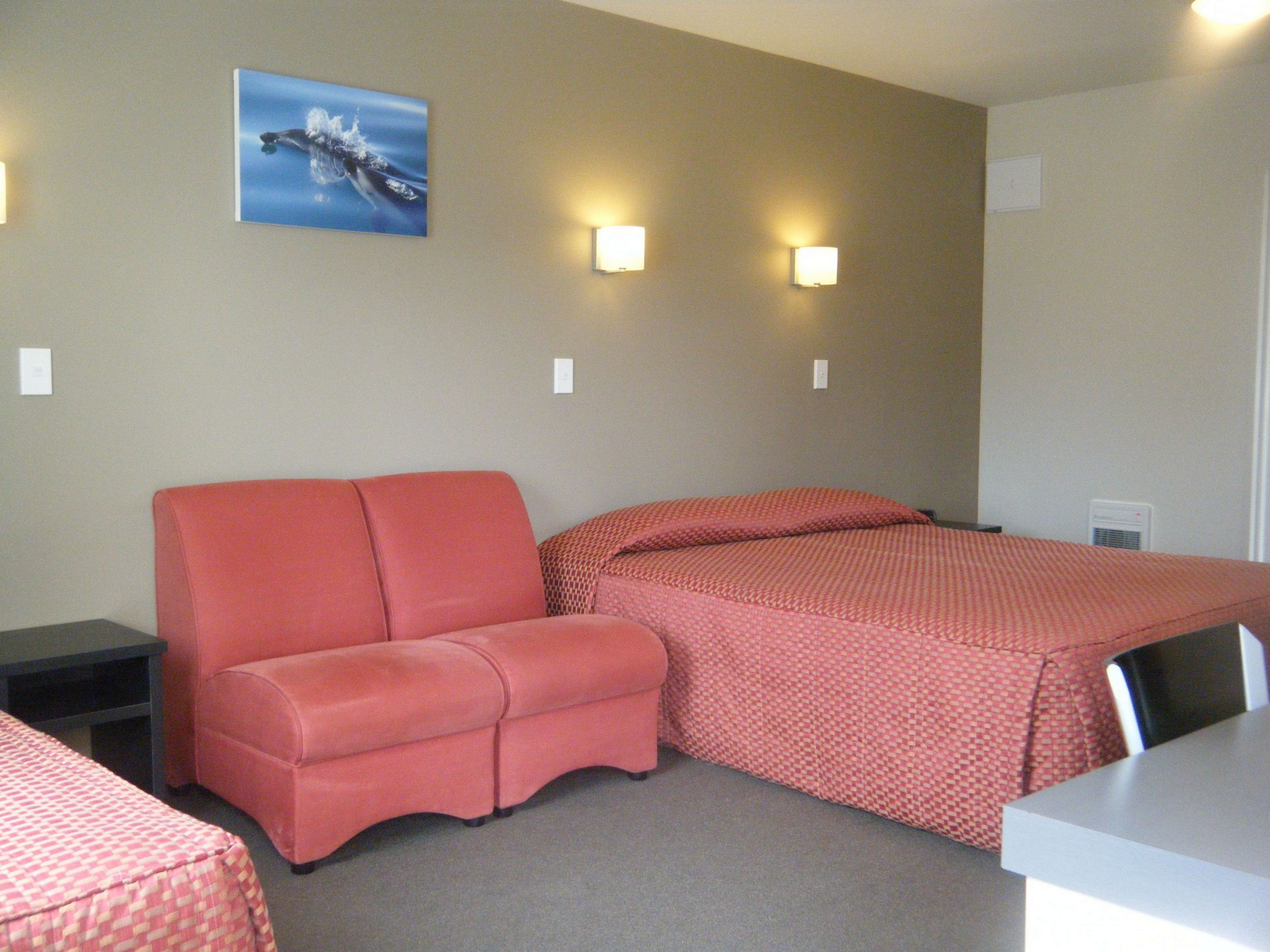 A hotel room with a single bed, a sofa, a desk, and a wall-mounted picture.
