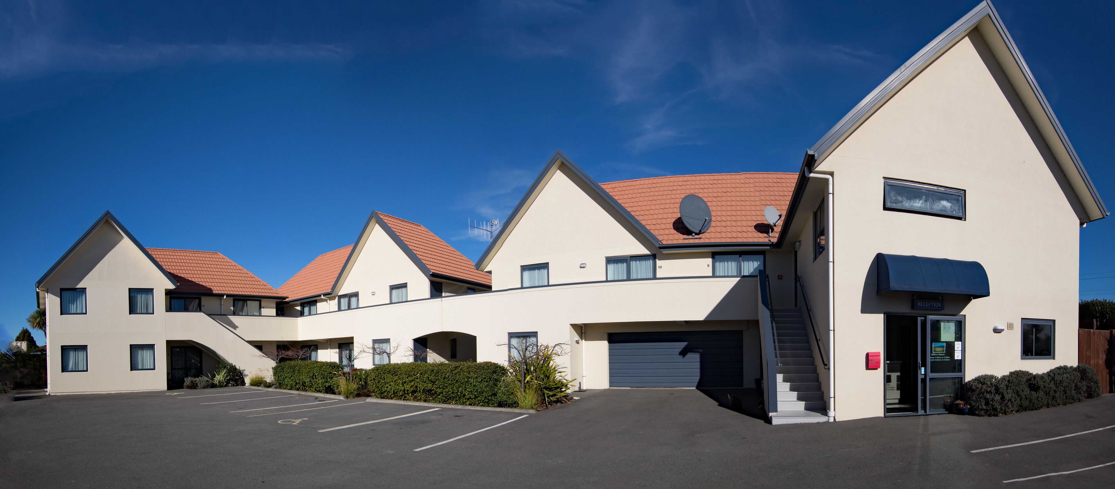 A modern building with a parking lot, a reception area, and multiple units with red roofs.