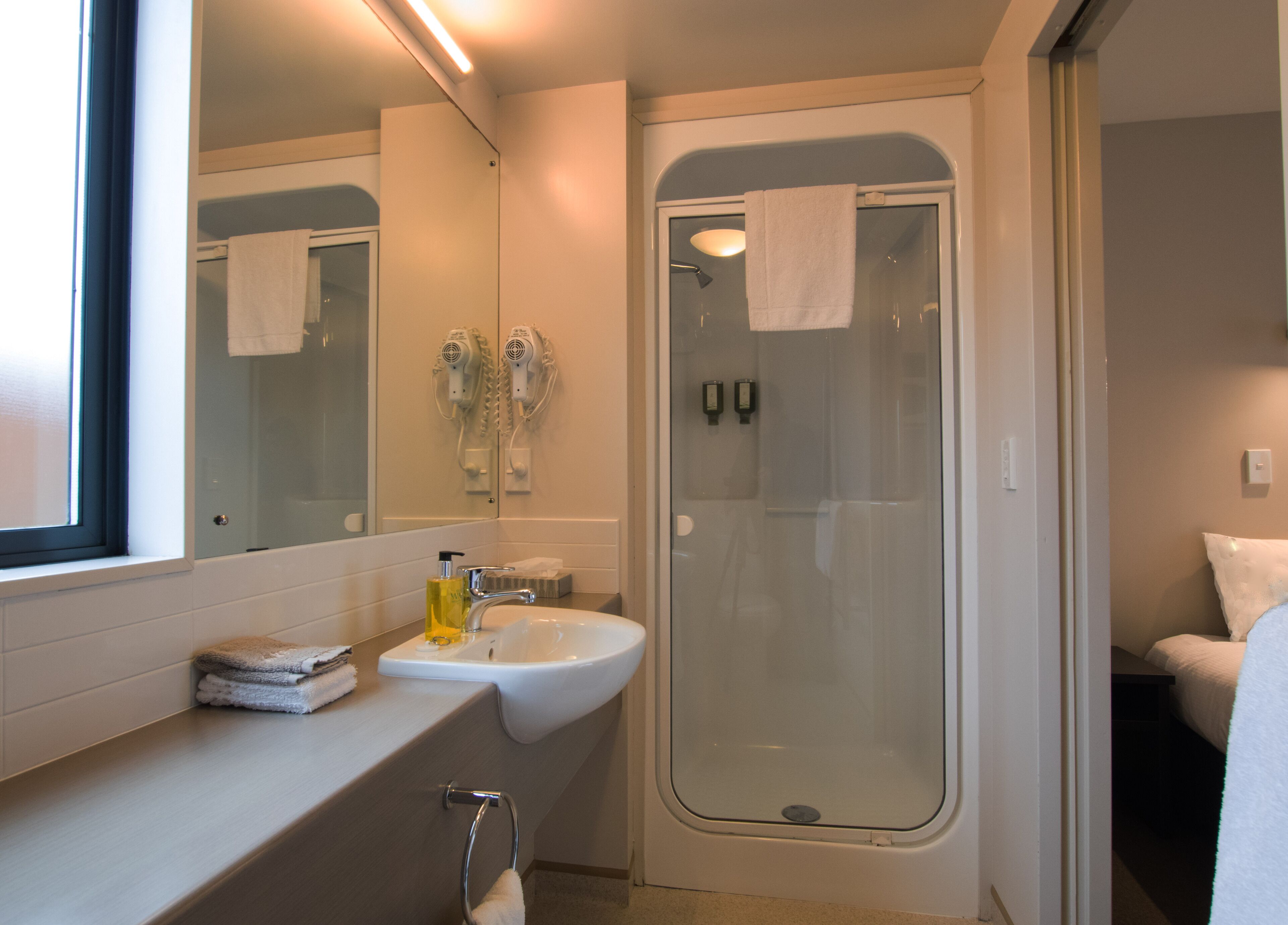 Un baño moderno con lavamanos, espejo y ducha con mampara de vidrio.