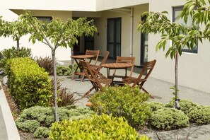 Un patio con mobiliario exterior y diversas arbustos y árboles pequeños.