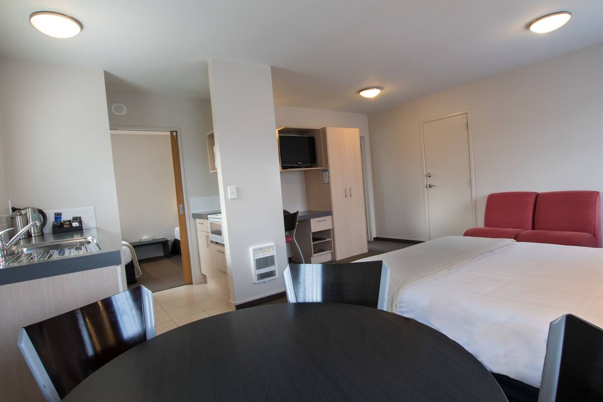A hotel room with a bed, a desk with a chair, a TV, and a red couch.
