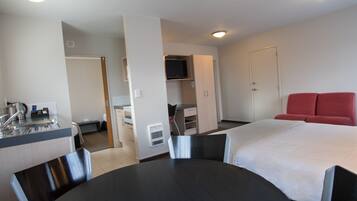 A hotel room with a bed, a desk with a chair, a TV, and a red couch.