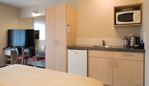 A compact hotel room with a bed, a small kitchenette, a microwave, a sink, and a television.
