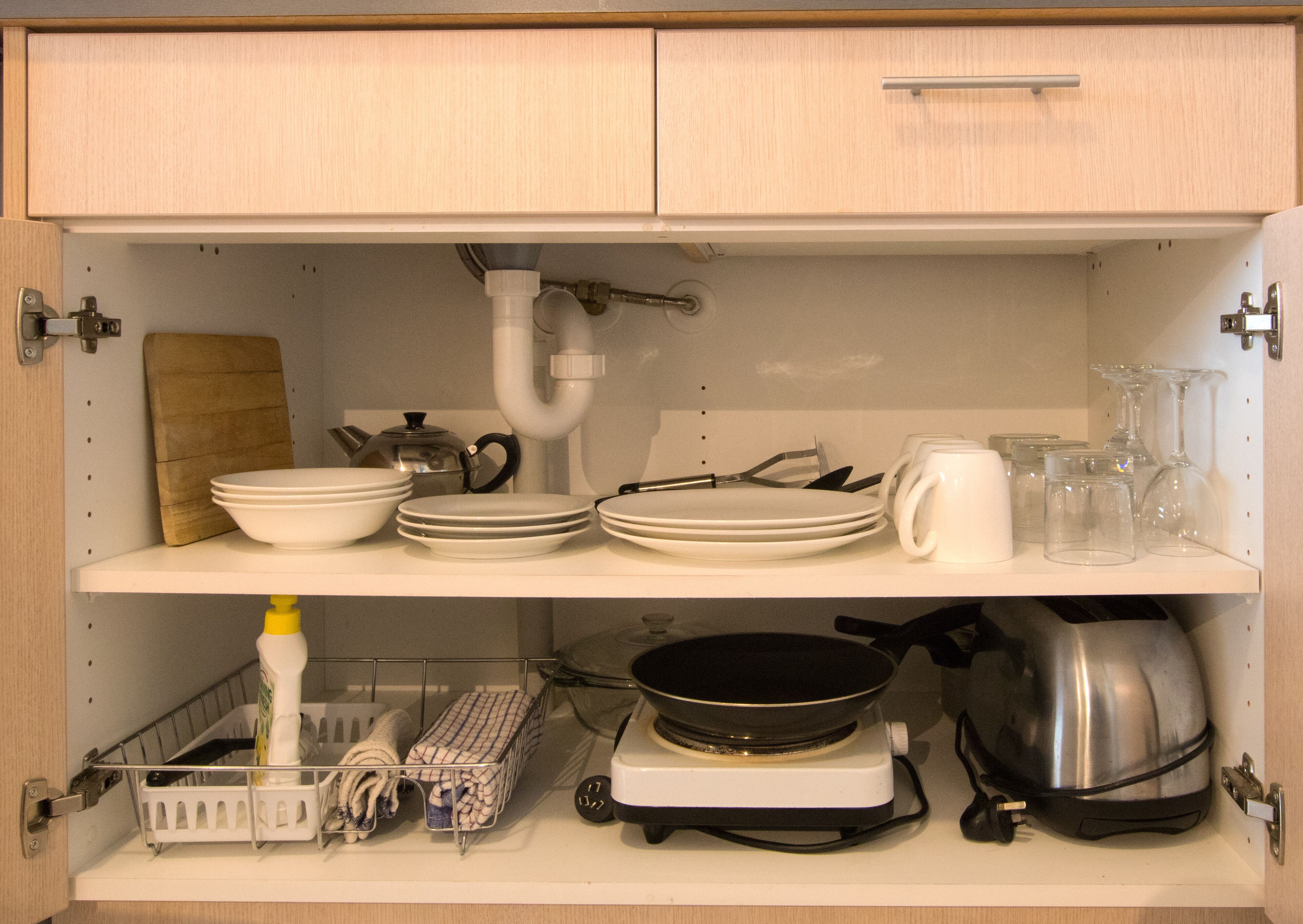Une cuisine avec des meubles blancs, une cuisinière, une poêle, une bouilloire, ainsi que divers plats et ustensiles.