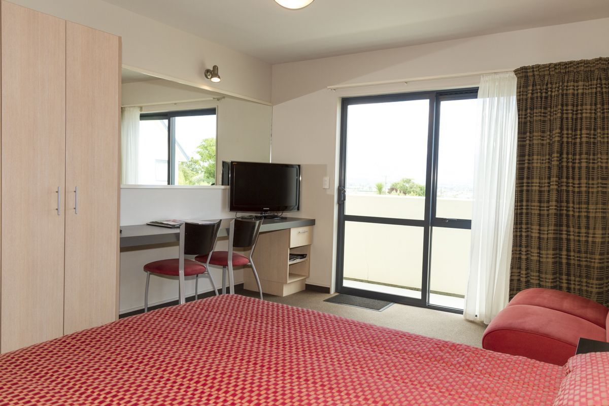 A hotel room with a bed, a desk with a chair, a television, and a sliding glass door to the outside.