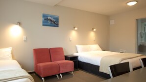 A hotel room with two beds, a red chair, a desk, and a painting on the wall. - Bella Vista Motel Kaikoura (Kaikoura)