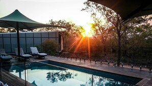 A pool area with lounge chairs and a glass barrier. - Cicada Lodge (Nitmiluk)