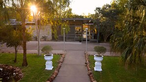 A pathway leading to a building with a glass facade, surrounded by greenery and a small water feature. - Cicada Lodge (Nitmiluk)