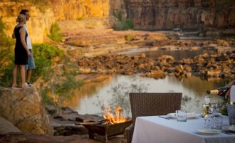 Comedor con mesa lista para dos, con vista a un río y un pozo de fuego.