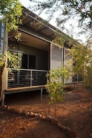 Una casa moderna con balcón, un jardín pequeño y una valla de metal.