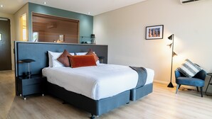 A modern bedroom with a large bed, bedside tables, a chair, and a wall-mounted shelf. - Cicada Lodge (Nitmiluk)