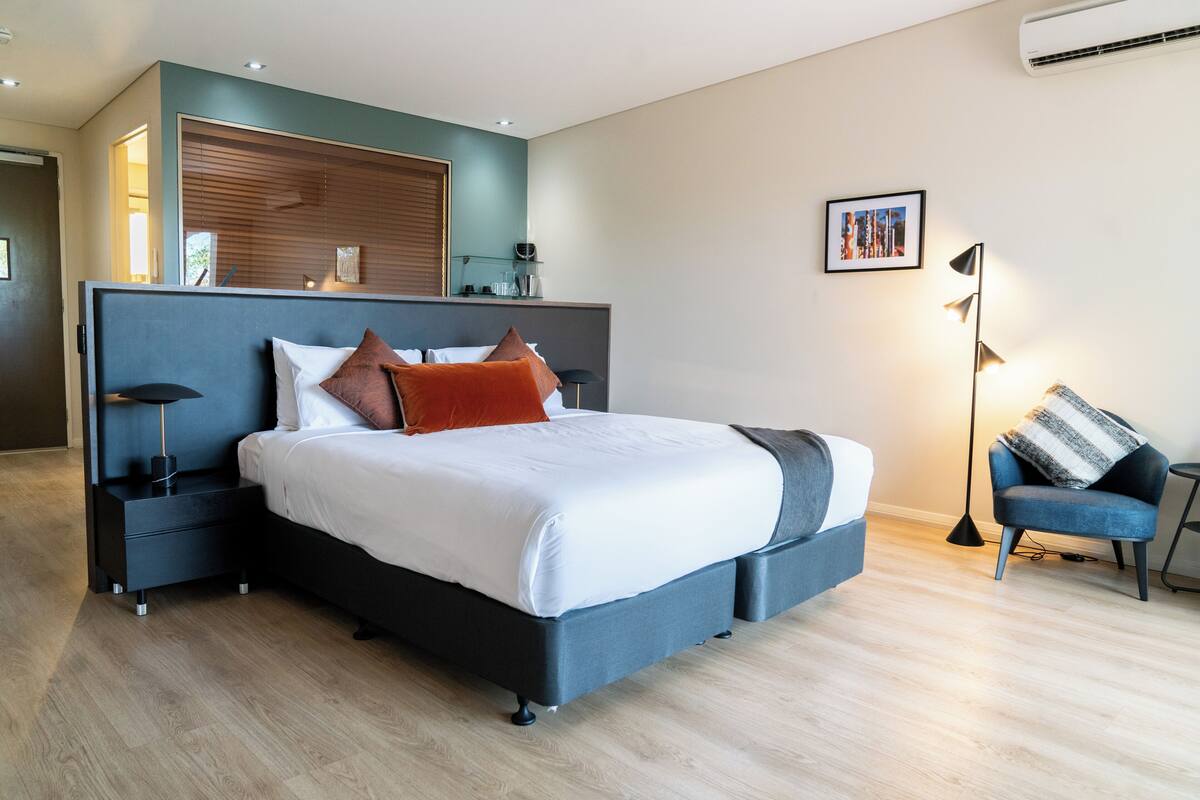 A modern bedroom with a large bed, bedside tables, a chair, and a wall-mounted shelf.