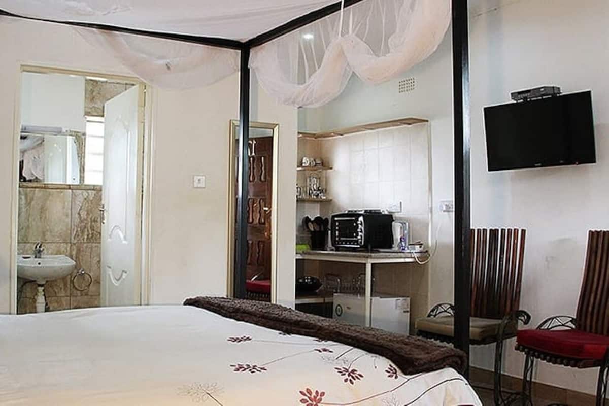 Un dormitorio con cama, escritorio, silla, televisión y baño visible a través de una puerta abierta.
