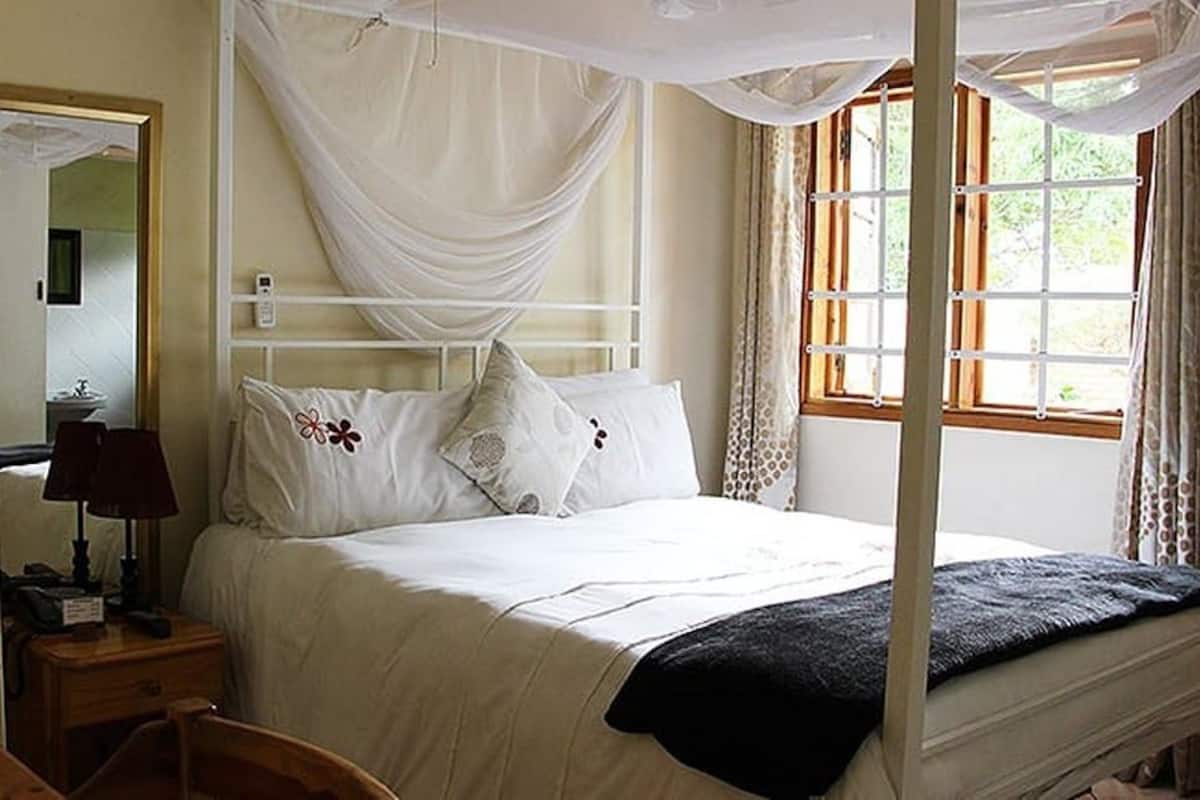 Un dormitorio con una cama con dosel, una mesita de noche con lámpara y una ventana con cortinas.