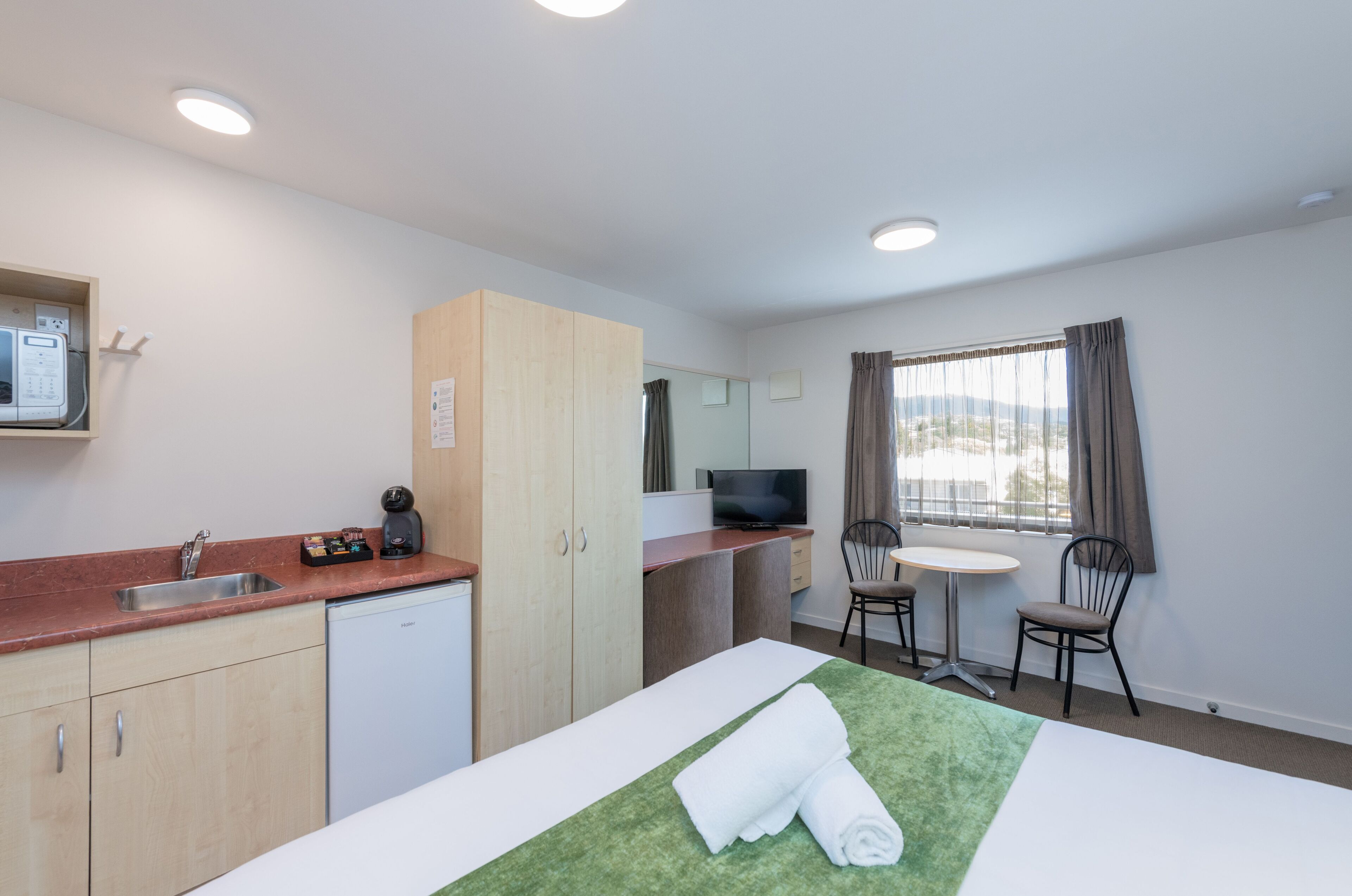 A hotel room with a bed, a desk, a chair, a television, a sink, and a microwave.