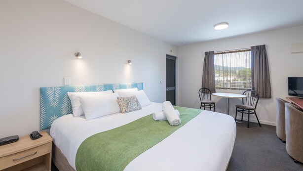 A hotel room with a bed, bedside table, chair, desk, and a window with curtains. - Bella Vista Motel Nelson (Nelson)