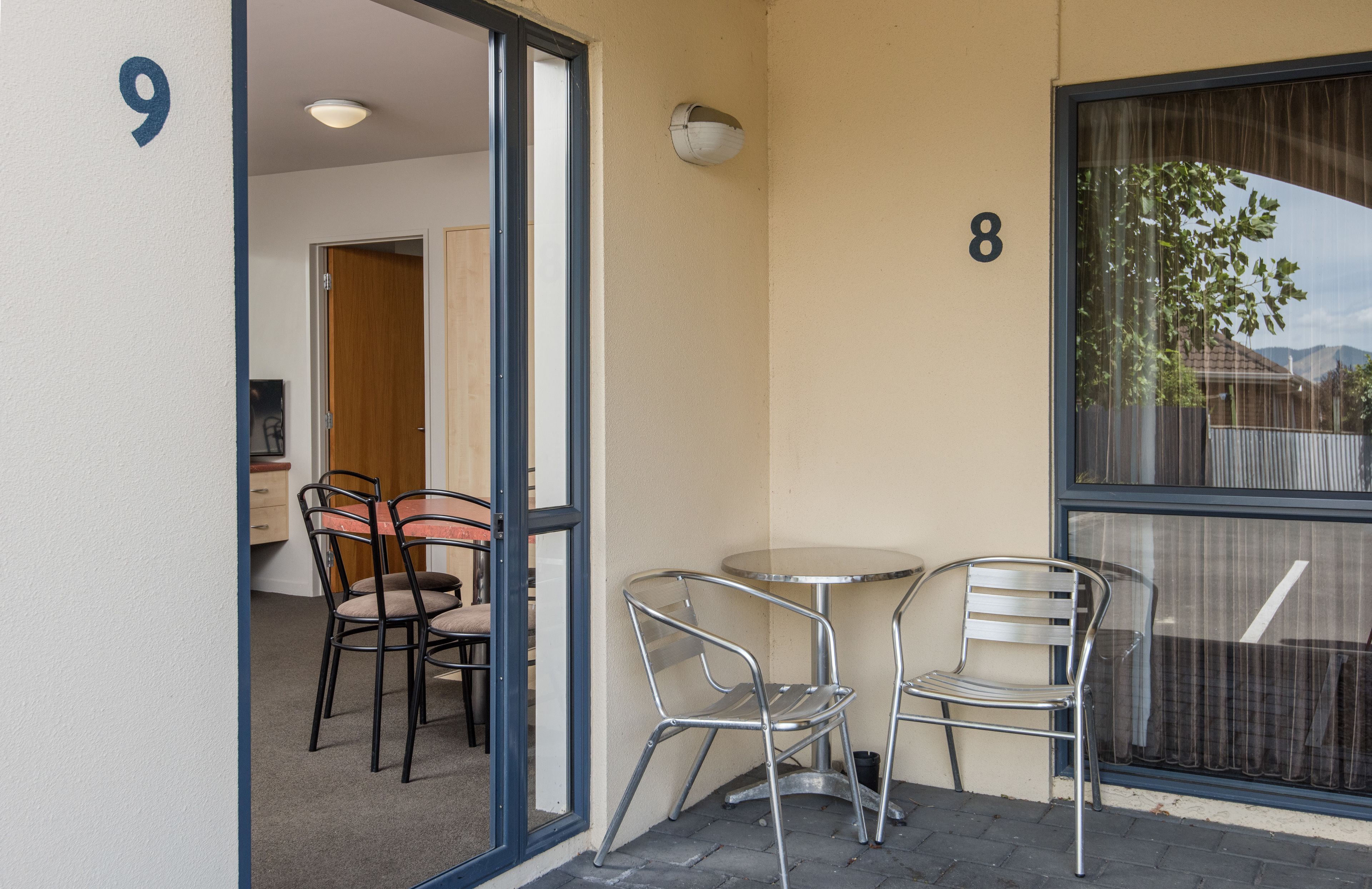 A small outdoor seating area with metal chairs and a table, adjacent to a building with the number 9 on the wall.