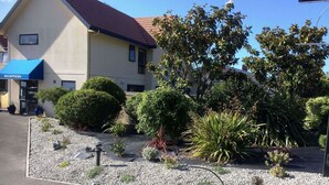 Un hôtel doté d’une réception, d’un jardin aménagé avec différentes espèces de plantes et d’un chemin en gravier, ainsi que d’un bâtiment surmonté d’un toit rouge.