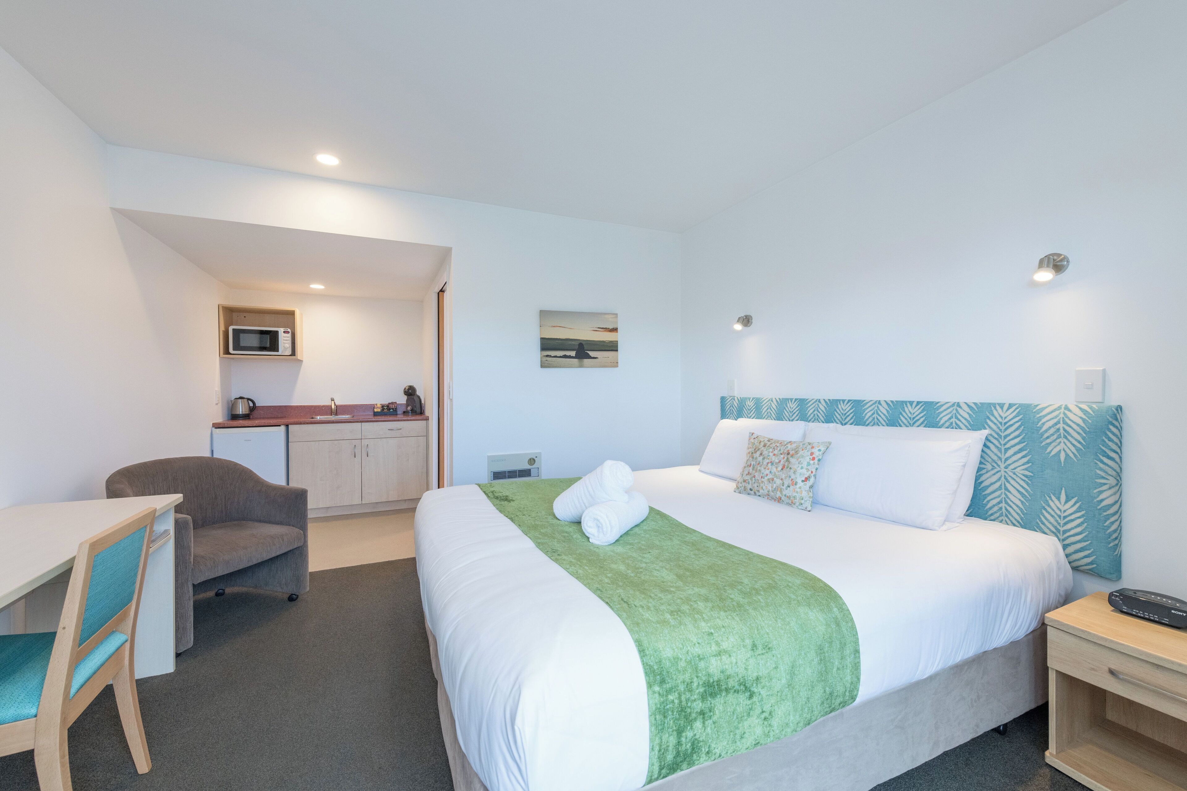 A hotel room with a bed, a desk, a chair, a microwave, and a small kitchenette.