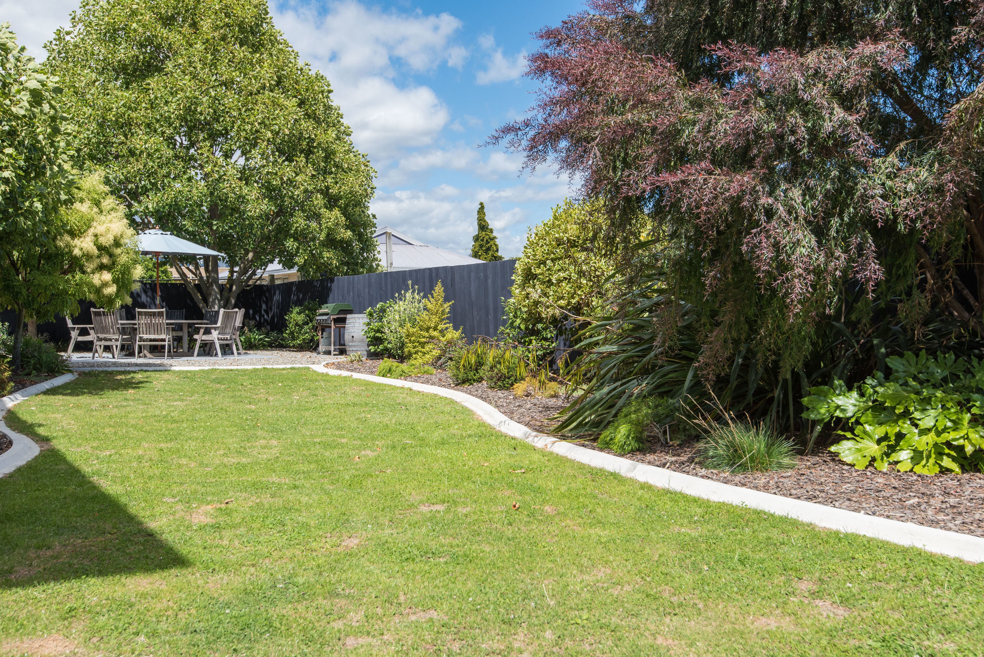 A well-maintained backyard with a lawn, patio furniture, and various plants.