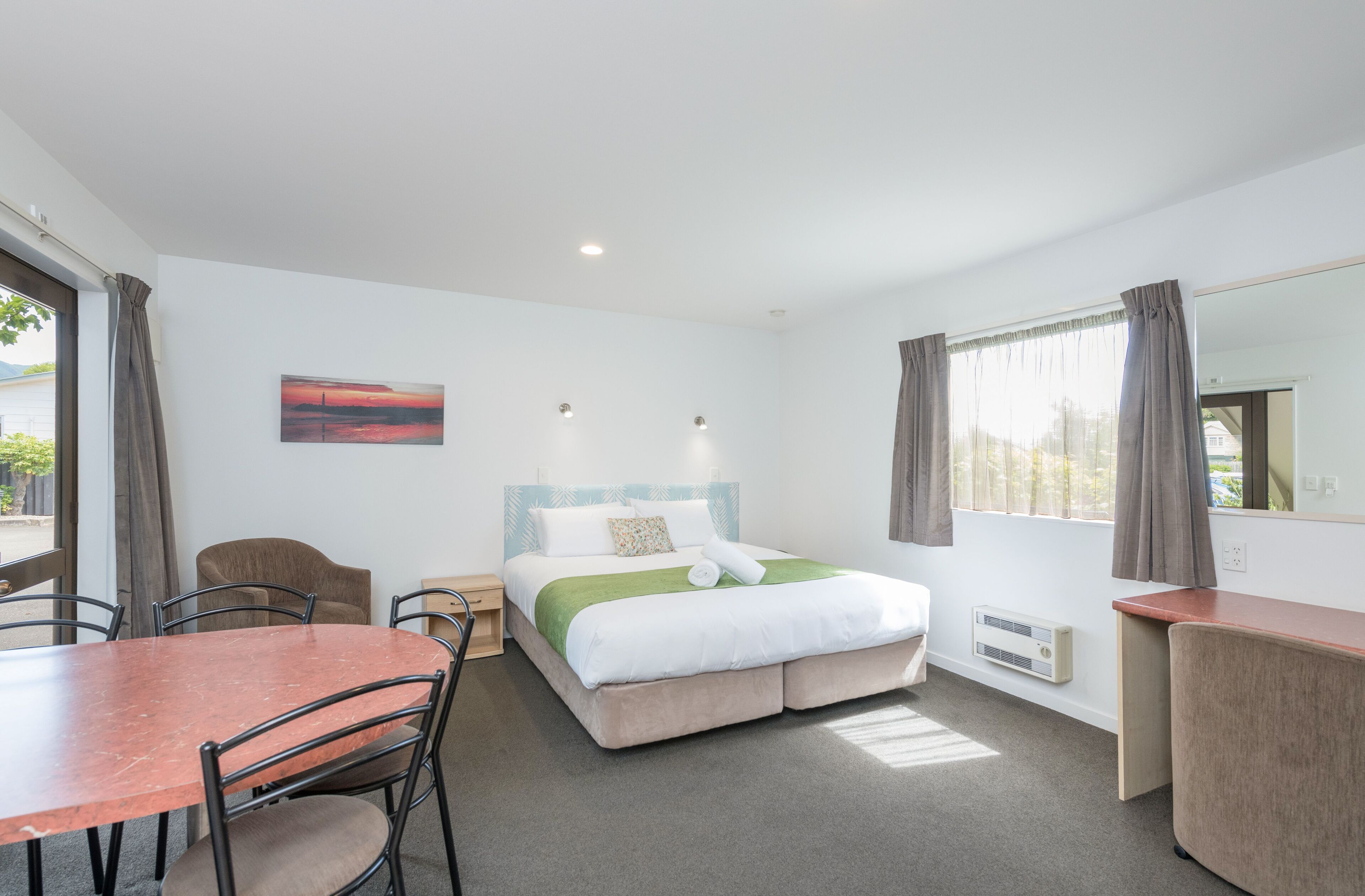 Quarto de hotel com cama, escrivaninha, cadeira, mesa e um quadro na parede.