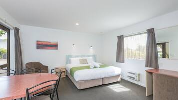 Quarto de hotel com cama, escrivaninha, cadeira, mesa e um quadro na parede.