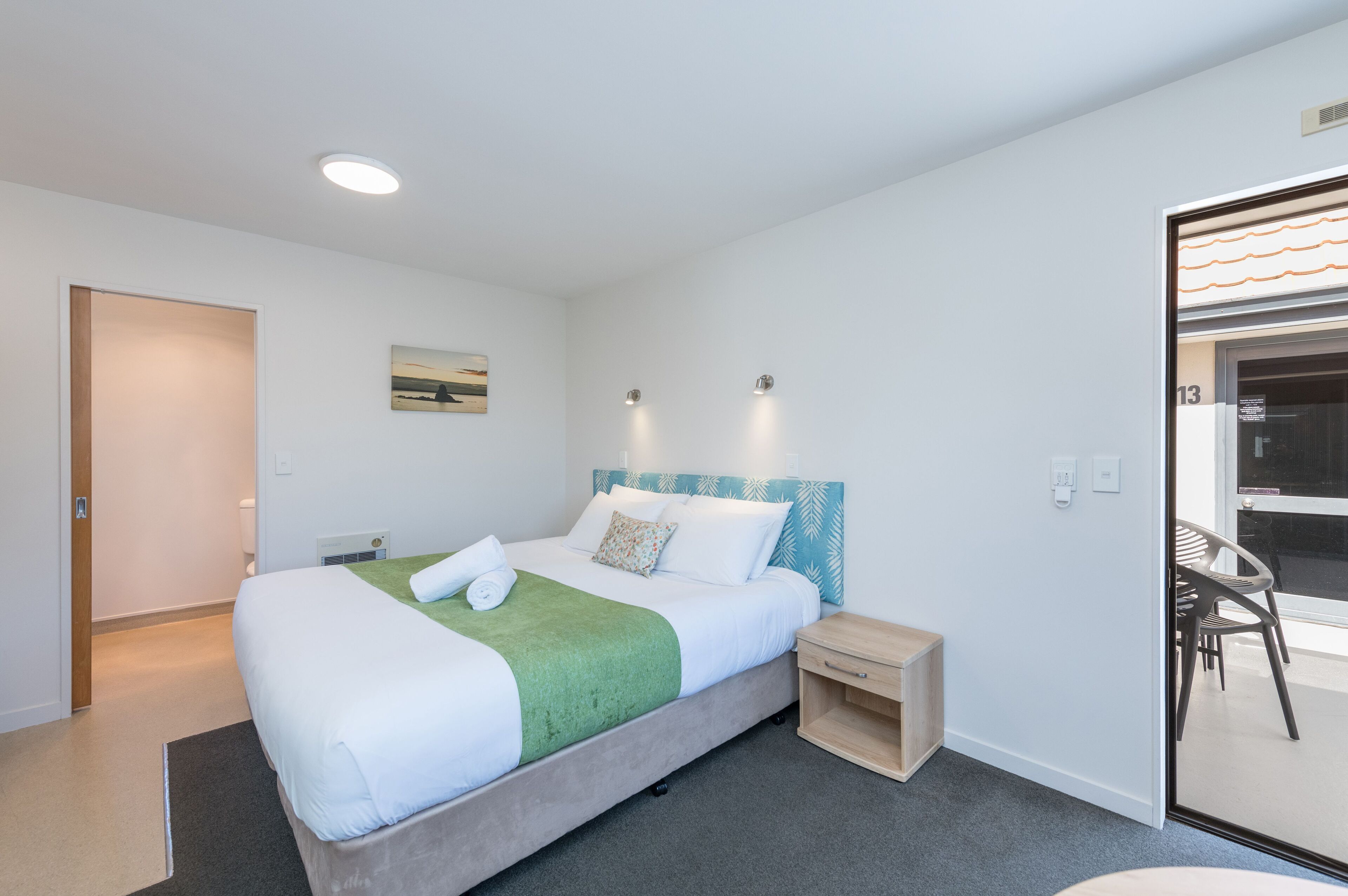 Ein modernes Hotelzimmer mit einem großen Bett, einem kleinen Nachttisch, einem Sessel und einer Glastür, die auf einen Balkon führt.