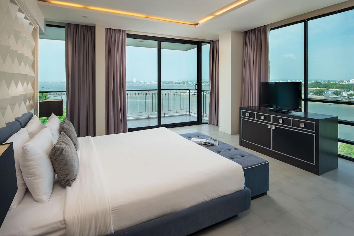 A modern bedroom with a large bed, a TV, and a balcony with a city view.