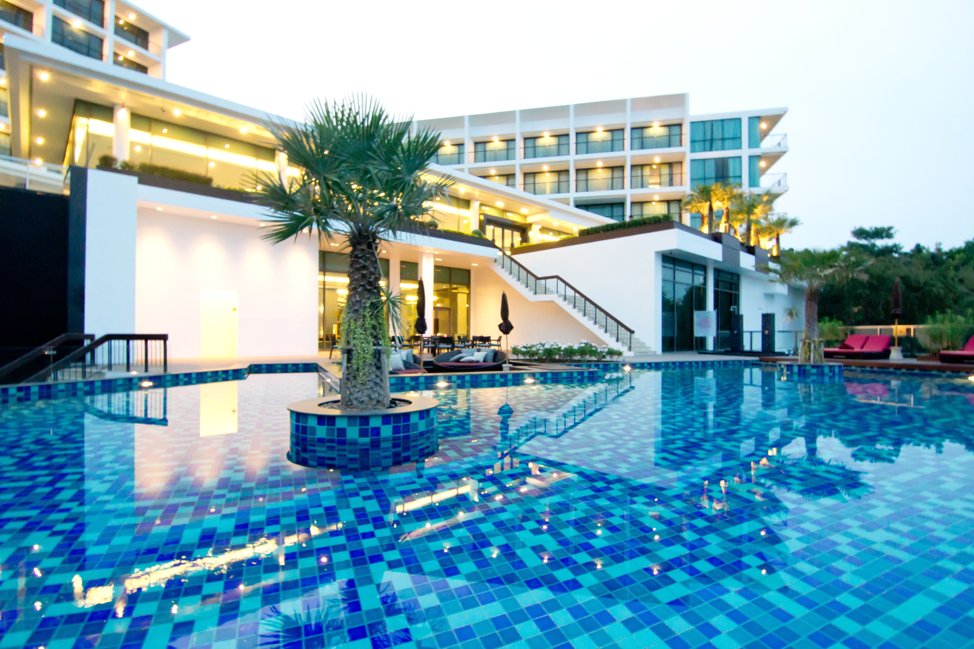 Een modern hotel met een zwembad, een palmboom en een trap naar de bovenverdiepingen.