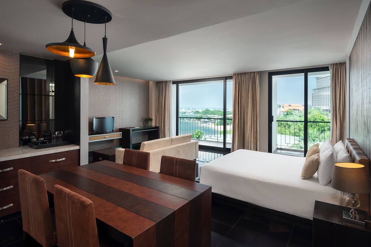 A modern hotel room with a large bed, a dining area, and a balcony with a view of the city.