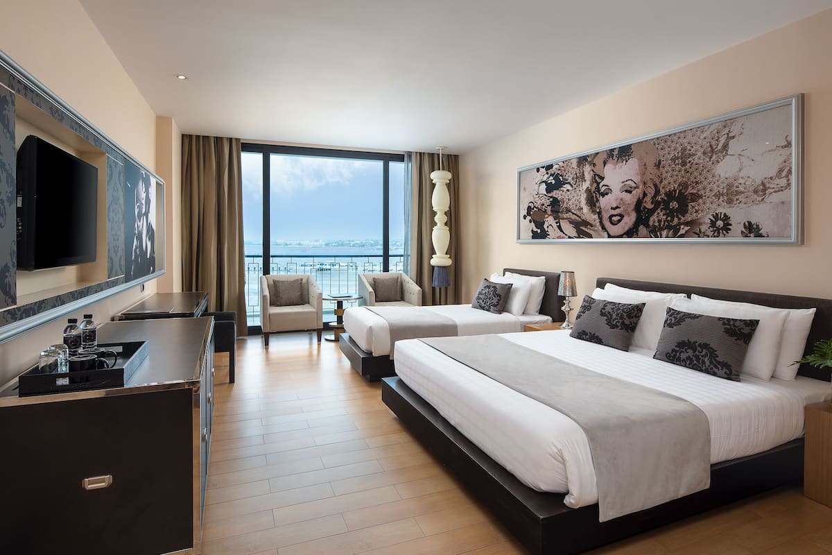 A hotel room with two beds, a TV, a desk, and a large window with a view.