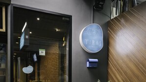 A modern building entrance with a glass door, a potted plant, and a sign that reads "TIRAJ". - TIRAS Patong Beach Hotel (Patong)