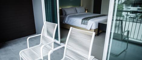 A modern hotel room with a bed, two white chairs, a large window, and a view of the outside.