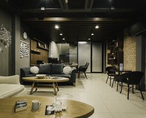 Een moderne woonkamer met een bank, salontafel en stoelen. Er is een keuken met een koelkast en een magnetron.