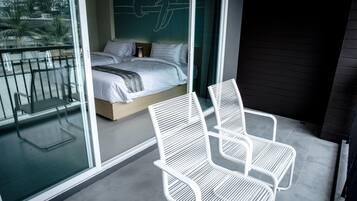 Un balcon avec un lit, des chaises blanches et un mur de verre donnant sur l’extérieur.