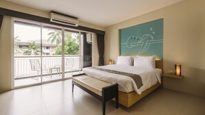 A bedroom with a bed, a bench, a balcony with chairs, and a view of palm trees and buildings. - TIRAS Patong Beach Hotel (Patong)