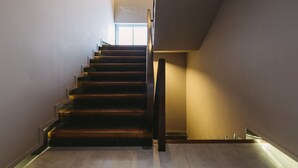 A modern staircase with wooden steps and a metal railing, leading to a bright room with a window. - TIRAS Patong Beach Hotel (Patong)