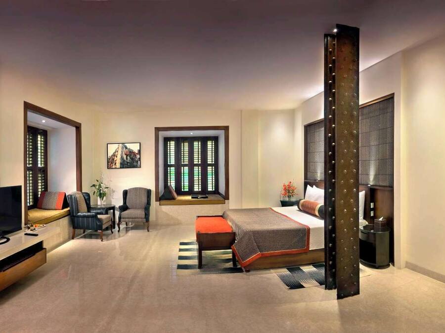 A modern hotel room with a bed, seating area, TV, and large windows.