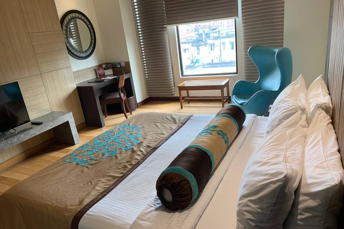 Ein Hotelzimmer mit einem großen Bett, einem Schreibtisch, einem Sessel und einem Fenster mit Blick auf die Stadt.